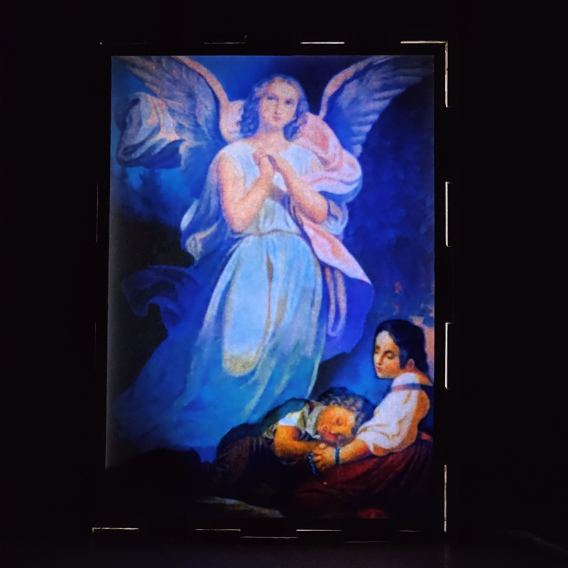 Lámpara con doble imagen  (Ángel de la guarda), vista encendida, donde se revela la ilustración completa al encender la luz LED.