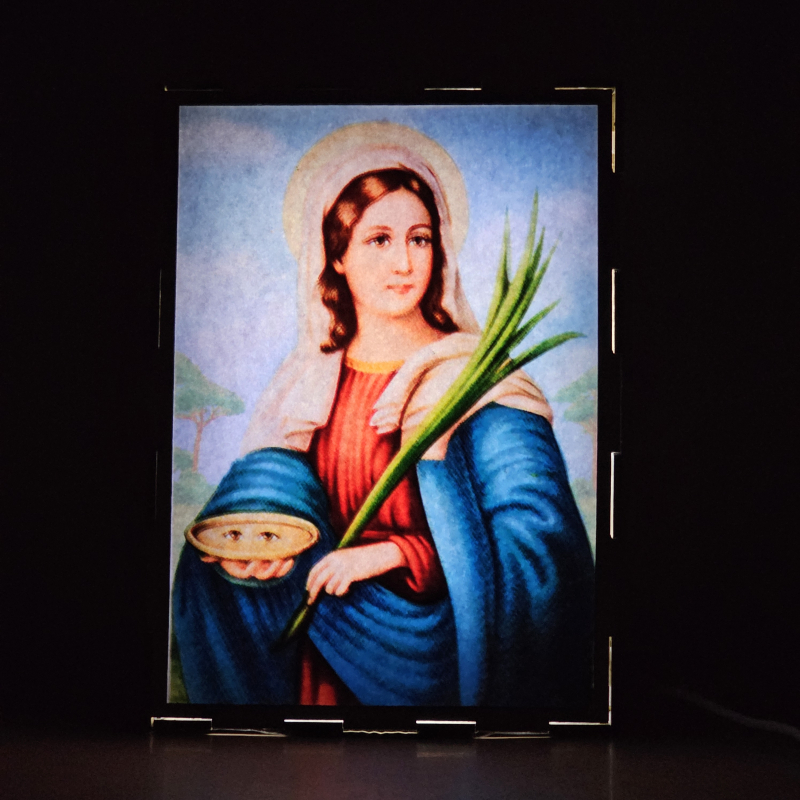 Lámpara con doble imagen  (Santa Lucía), vista encendida, donde se revela la ilustración completa al encender la luz LED.