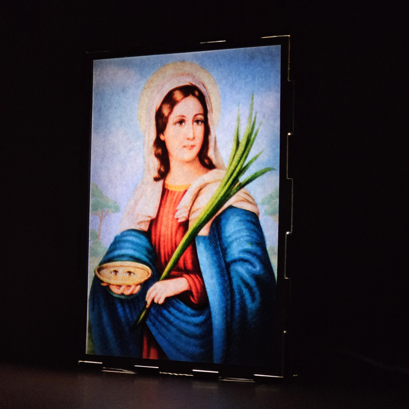 Lámpara con doble imagen  (Santa Lucía), vista encendida, donde se revela la ilustración completa al encender la luz LED.